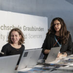 Zwei Personen am Empfang einer Veranstaltung hinter Laptops und Stehtisch mit vielen Flyern.