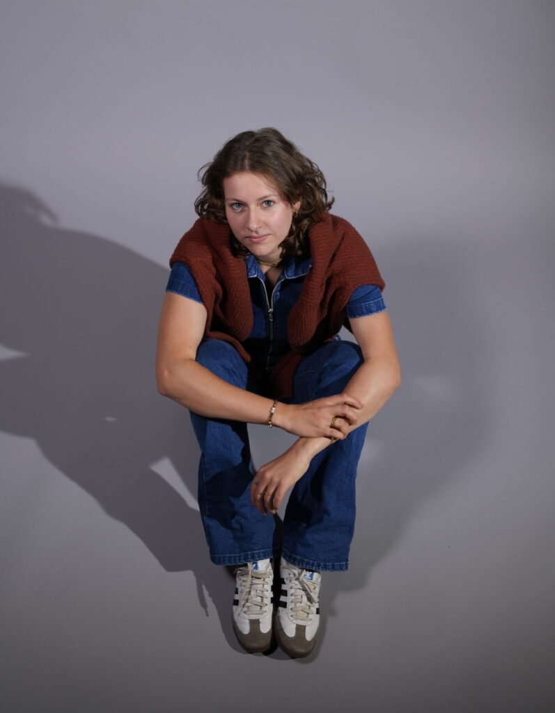 Ganzkörperfoto einer Person, die in Jeansonesie am Boden hockt und nach oben blickt.