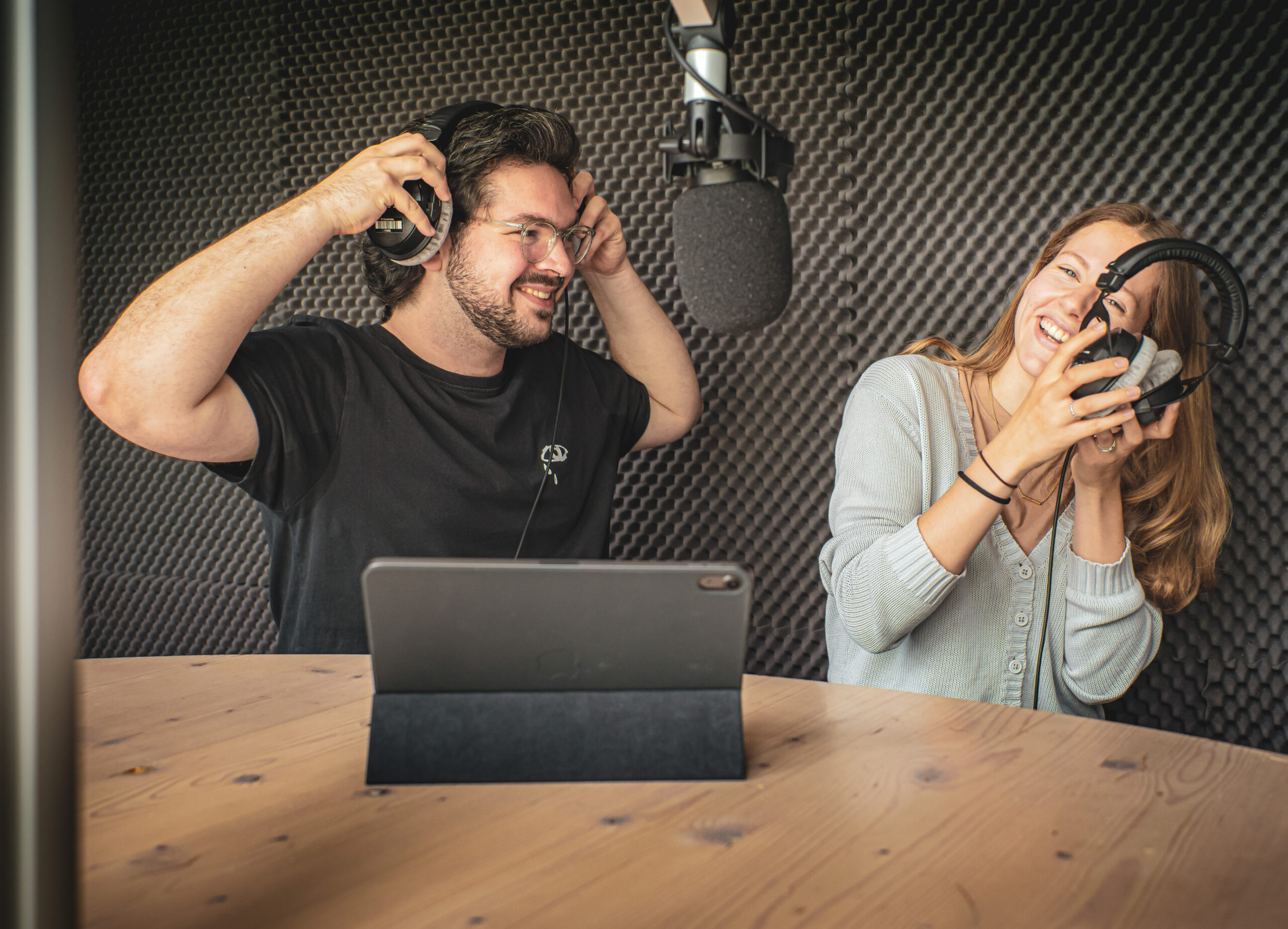 Zwei Personen bei der Aufnahme eines interaktiven Hörspiels mit Kopfhörern auf vor einem Mikrofon dem Skript.