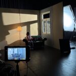 Person, die auf dem Sofa im Filmset sitzt und durch ein Fenster durch das künstliche Mondlicht angestrahlt wird.