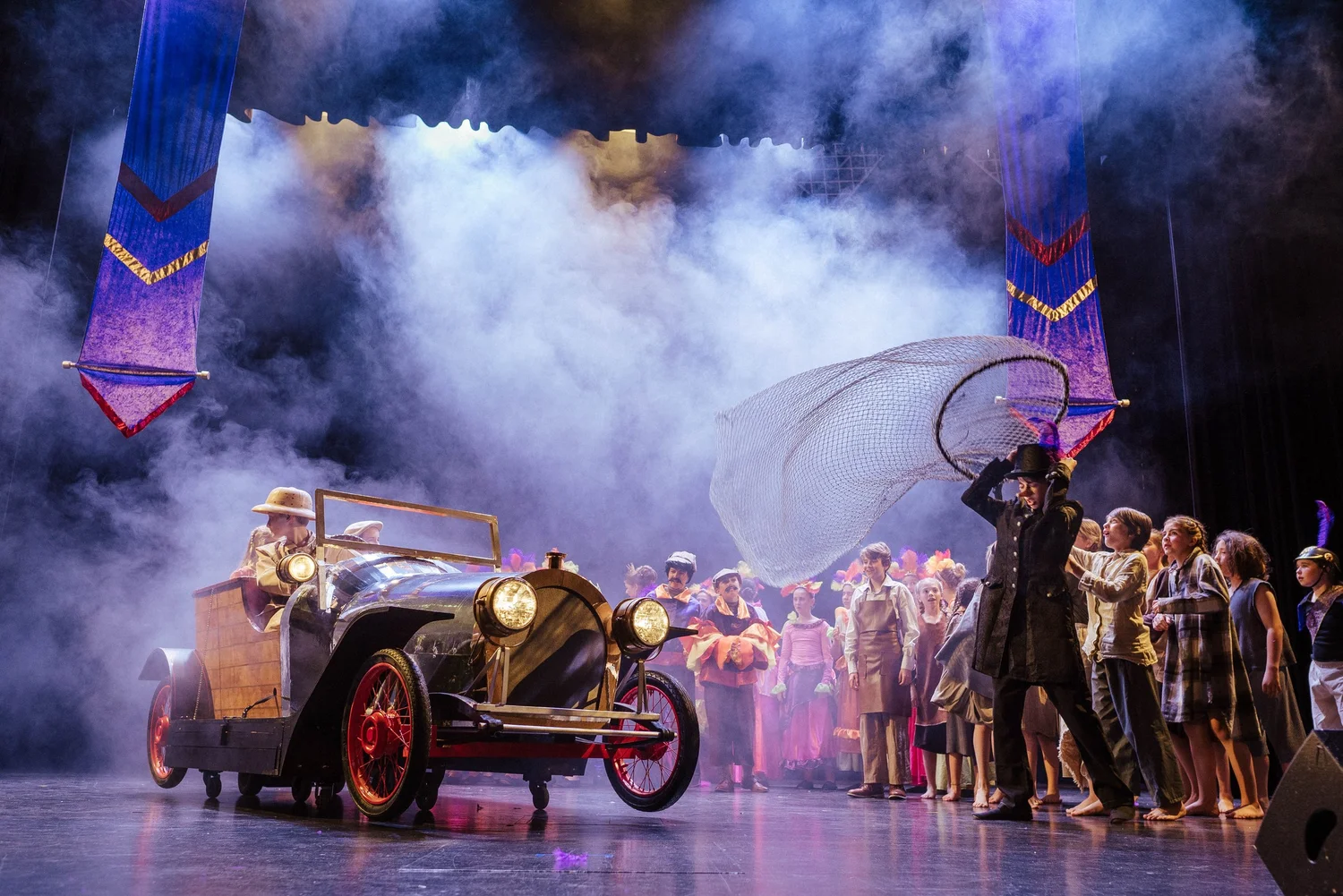 Eine Muscialbühen voller Kinder und Jugendlichen auf der das Auto Tschitti fährt und vor dem Kinderfänger flüchtet.