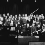 Schwarzweisses Gruppenfoto einer TV-Produktions-Crew vor einer Kamera.