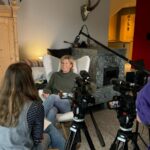 Ein Videointerview-Setup mit der Protagonistin in einem Sessel, gegenüber von ihr sitzt die Interviewerin.