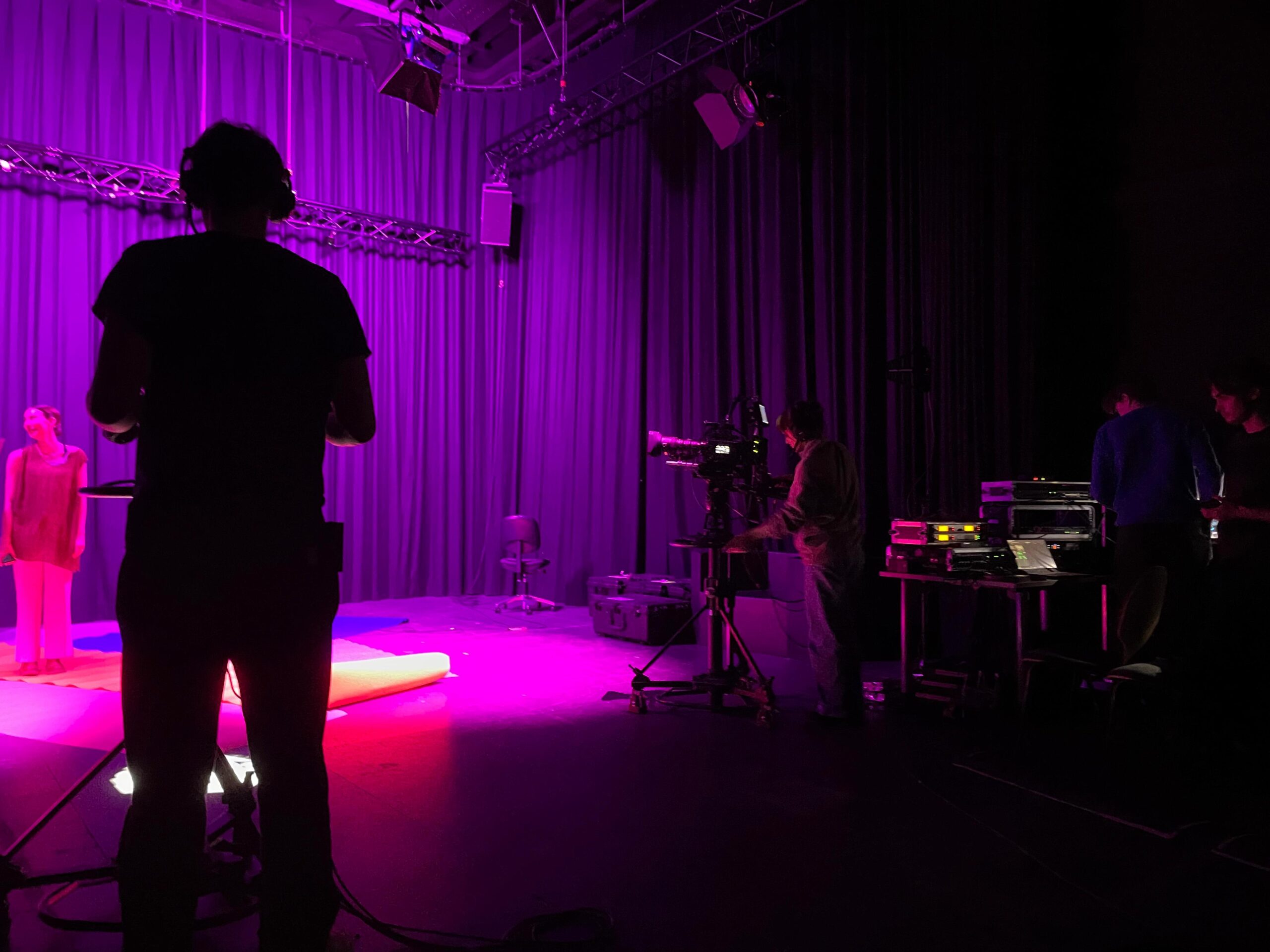 Ein TV-Set in pinkem Licht mit Moderatorin, die von zwei mobilen Kameras gefilmt wird.