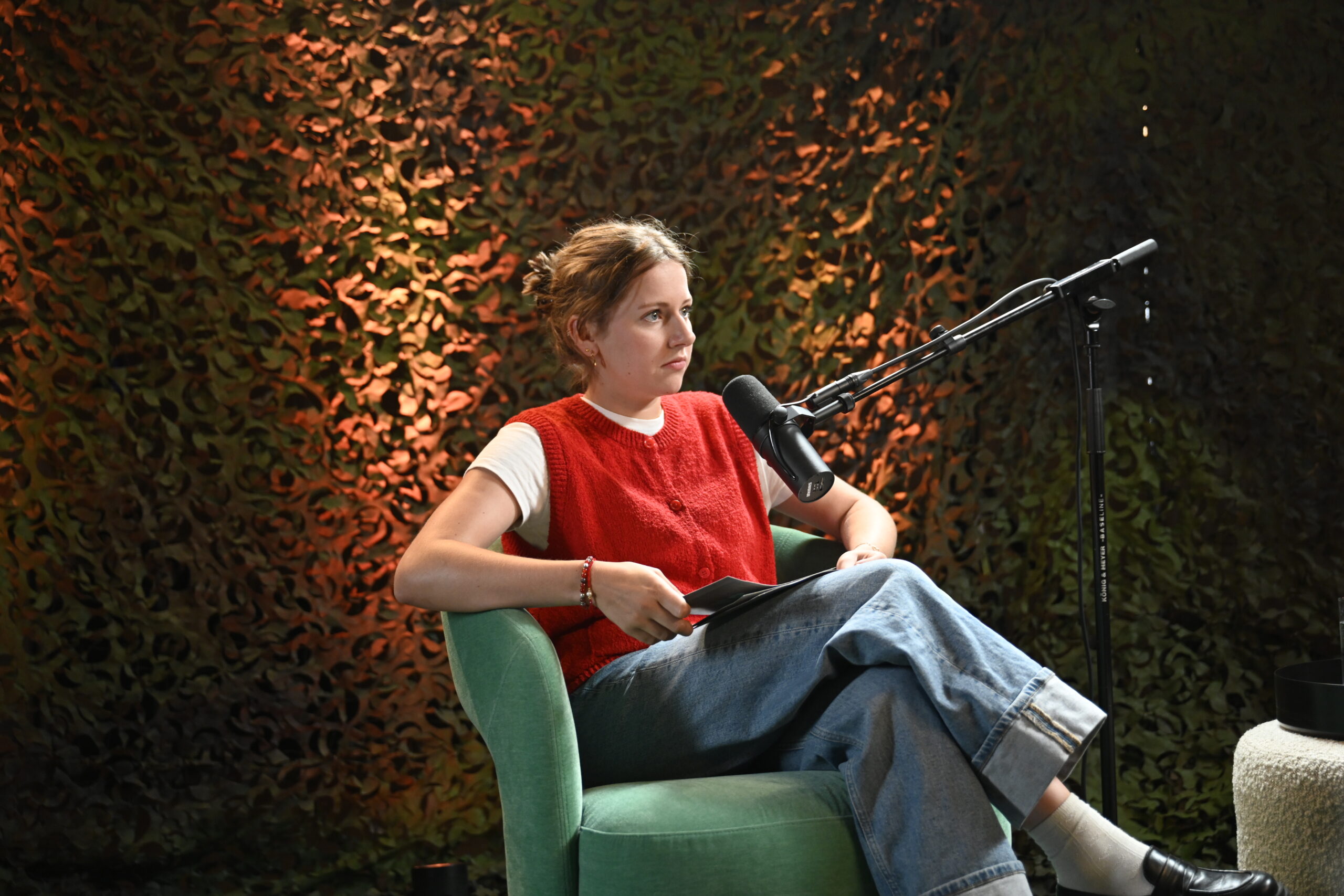 Podcastmoderatorin, die in einem Sessel mit Moderationskarten vor dem Mikrofon sitzt und der Gästin zuhört.