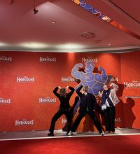 Drei Freundinnen vor einer Fotowand in sportlicher Pose passend zu der Herkules Figur.